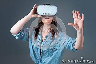 Emotional young woman using a VR headset and experiencing virtual reality on grey background Stock Photo