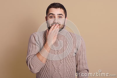 Emotive positive young male covering mouth, trying to stop laughter or hide smile, hearing something hilarious while stands over Stock Photo