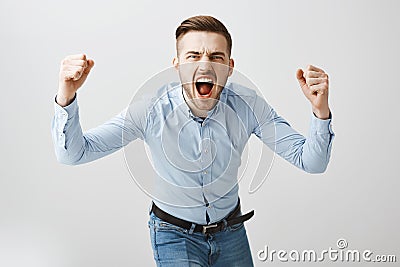 Emotive thrilled concerned european male boss in formal blue shirt and jeans bending towards camera yelling and raising Stock Photo