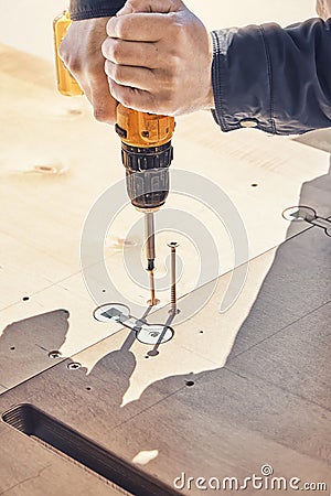 Employee assembles dining table with electric screwdriver outdoors Stock Photo