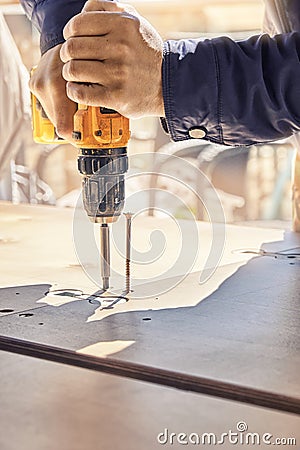 Employee assembles dining table with electric screwdriver outdoors Stock Photo