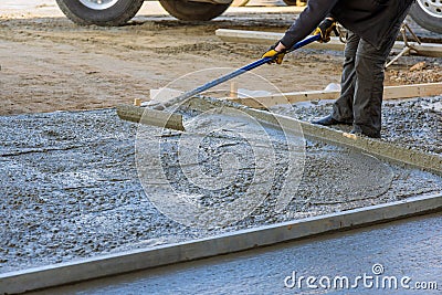 An employee of a construction company leveled a wet concrete sidewalk with the use of long trowels after pouring Stock Photo