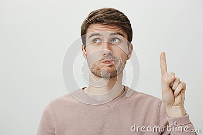 Employee has suggestion. Portrait of handsome european male student raising index finger and looking up with puckered Stock Photo
