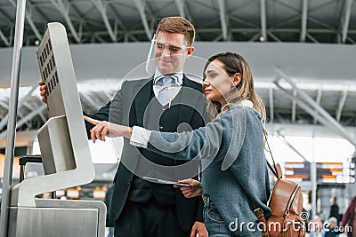 Employee helping to use terminal. Young female tourist is in the airport at daytime Stock Photo