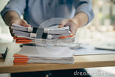 An employee sits at a table full of paper. stamp on the pile of unfinished documents A young account manager`s secretary works in Stock Photo