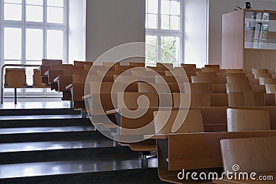 Empty auditorium at university with wooden chairs and banks and large windows and stairs on one side. Stock Photo