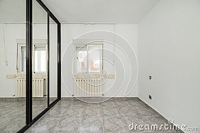 An empty bedroom with a custom built closet with black metal edged sliding mirror doors, a varnished sapele wood access door and Stock Photo