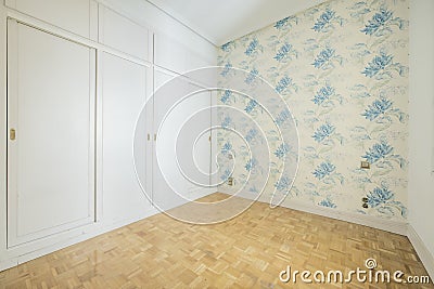 Empty bedroom with white wooden venetian style door cabinet on one wall, walls with blue patterned wallpaper and light oak parquet Stock Photo