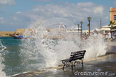 An empty bench stands on the edge of the embankment of Chania about which waves and a lot of splashes beat Editorial Stock Photo