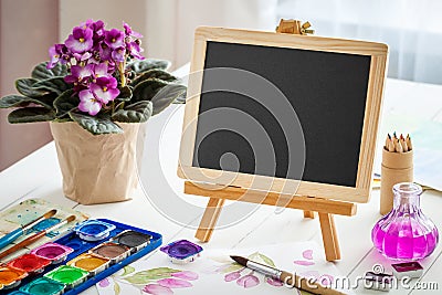 Empty blackboard, flower in pot and watercolor paints Stock Photo