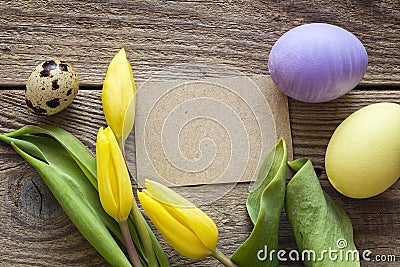 Empty brown card, Easter eggs and tulips on a old wooden table. Stock Photo