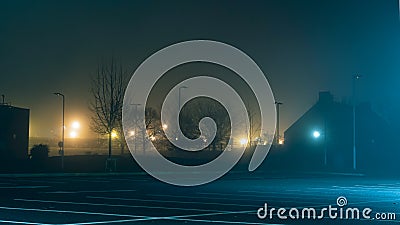 An empty car park with street lights glowing in the distance on a mysterious moody, foggy atmospheric winters night Stock Photo