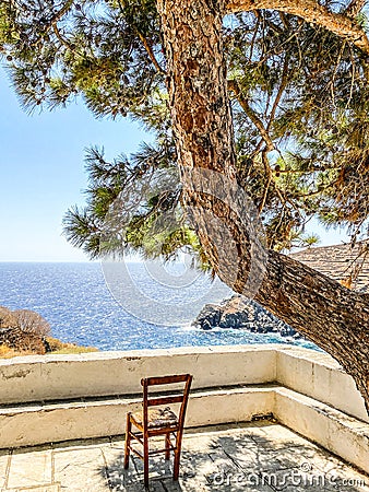 Empty chair on terrace in front of aegean sea under shadow of pine tree, Sifnos island, Greece Stock Photo