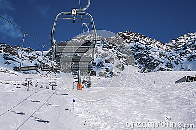 Empty chairlifts at ski resort against snowcapped mountains during sunny day Stock Photo