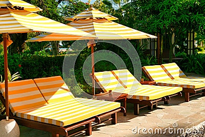 Empty chaise lounges with yellow-white striped mattresses that stand under a sun umbrella with the same pattern. Sanya, Hainan. Stock Photo