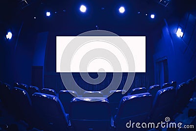 Empty cinema auditorium with empty white screen. Empty rows of theater or movie seats. Blue toned Stock Photo