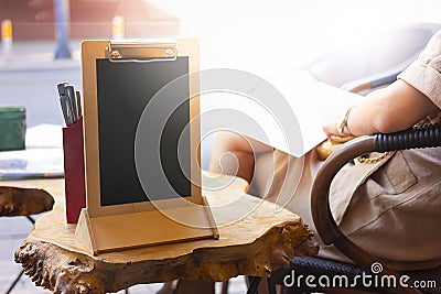 Empty clipboard stands on an unusual wooden table in a street cafe. Place for text, announcement or lettering Stock Photo