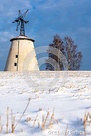 Empty Countryside Landscape in Sunny Winter Day with Snow Covering the Ground with Big Abandoned Windmill in Background Stock Photo