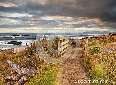 Empty foot path and wooden bridge on ocean beach trail with dark sky. Stock Photo