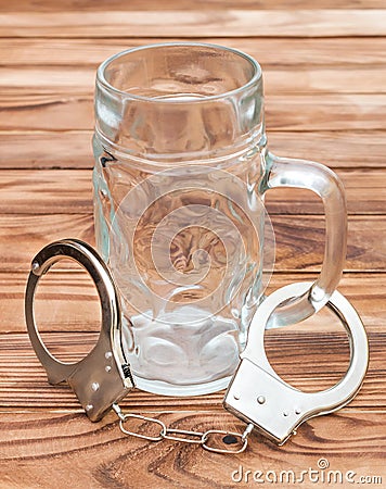 Empty glass for beer and handcuffs on wooden table. Alcohol dependence Stock Photo