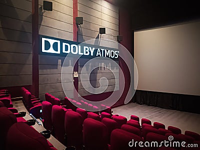 Empty Movie Theater With Dolby Atmos Sound System Display next to comfortable red seats and a large screen Editorial Stock Photo