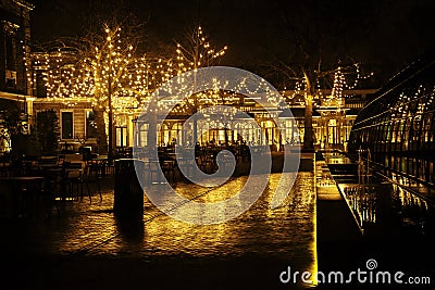 Empty night restaurant, lot of tables and chairs with noone, magic fairy lights on trees like christmas celebration Stock Photo