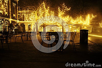 Empty night restaurant, lot of tables and chairs with noone, magic fairy lights on trees like christmas celebration Stock Photo