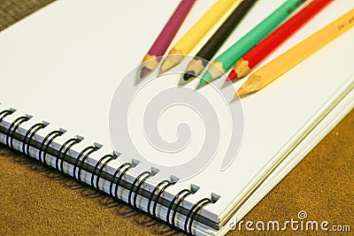 Empty notebook and colorful pencils on brown background, painting stuff Stock Photo