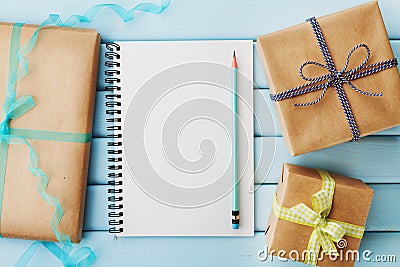 Empty notebook, pencil and gift or present box packed in kraft paper on blue wooden table Stock Photo