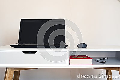 Empty open laptop with mockup and black screen on white desk table. Mouse. Book and cables. Stock Photo