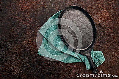 Empty oval cast iron frying pan and linen towel. Rusty dark background. Top view with copy space. Flat lay Stock Photo