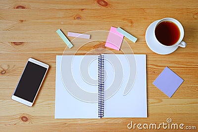 Empty pages opened notebook, smartphone, memo pad paper and a cup of hot tea on wooden working desk Stock Photo