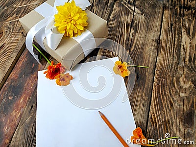 Empty paper blank with gift and flowers on wooden background. Stock Photo