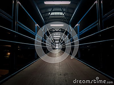 Empty pedestrian walkway illuminated with fluorescent tubes at night. Metallic structure over a road Stock Photo