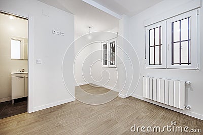 Empty room with laminate flooring, access to an en-suite bathroom and white aluminum windows with bars Stock Photo