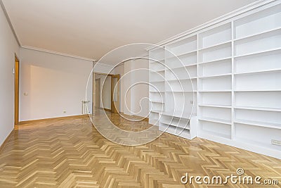 empty room with a wall covered with a white painted masonry bookcase, varnished and polished French oak parquet floors laid in a Stock Photo