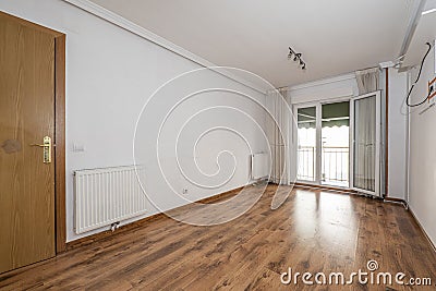 Empty room with wooden floor, plaster moldings on the ceiling, aluminum radiator, gray ceiling light, access to a terrace with Stock Photo