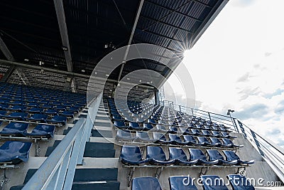 Empty Rows of stadium grandstand seats or stadium seats with sunray on roof and cloud sky, plastic blue and white seats on grand s Stock Photo