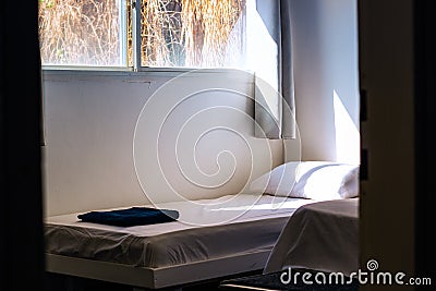 Empty rustic room of cheap hotel apartments with bed white sheet and morning sun light ray through window Stock Photo