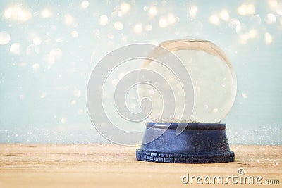 Empty Snow Globe over wooden table with glitter overlay. Magical Christmas concept. Copy space. Stock Photo