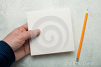 An empty square piece of paper in a man`s hand, a yellow pencil next to it. Mock-up Stock Photo