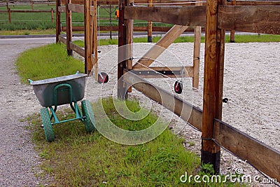 The empty stable. Empty open paddock for horse riding. Wheelbarrow for manure near an empty stable. Stock Photo