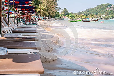 Empty sun lounge chairs under umbrellas standing close to seashore line during high tide water. Perspective view. Tropical Stock Photo