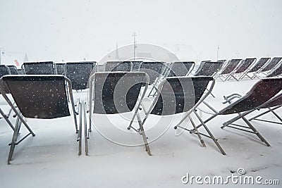 Empty sun lounger chairs out on a terrace during a Winter whiteout blizzard , Les Sybelles, France Stock Photo