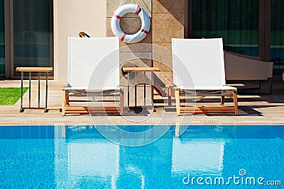 empty sunbeds near hotel and swimming pool and life buoy hanging on the wall Stock Photo