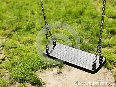 Empty swing on children playground. Green grass background. vacant chain swing for kids in a park. Corona virus causes empty Stock Photo