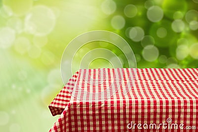 Empty table with red checked tablecloth over green bokeh background. Stock Photo