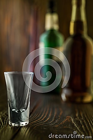 An empty tequila glass in front of many colorful liquor bottles, shallow depth of field, selective focus. Stock Photo