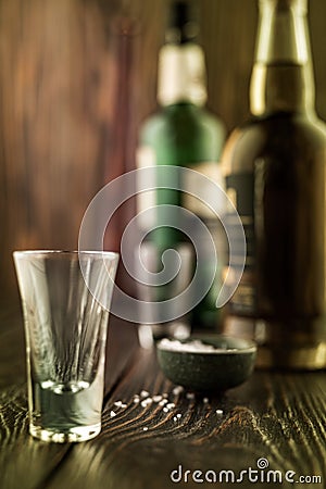 An empty tequila glass in front of many colorful liquor bottles, shallow depth of field, selective focus. Stock Photo