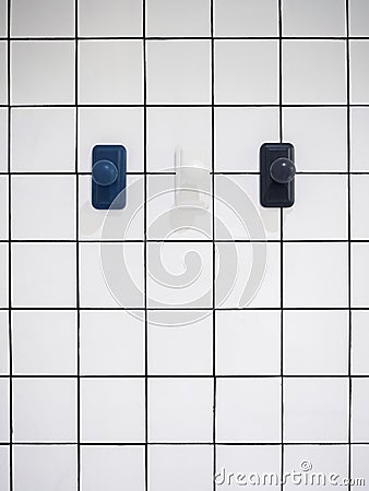 Empty three modern towel hooks, blue and white hanging on white grid wall bathroom. Stock Photo